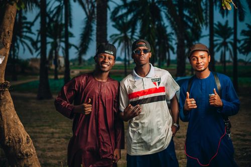 Free Three young men smiling and posing for the camera outdoors with palm trees in the background. Stock Photo