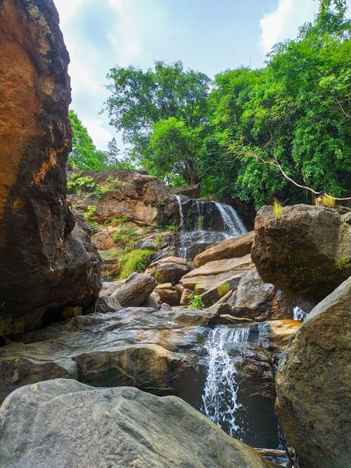 Free Serene waterfall cascading over rocks in a lush green forest, offering a soothing nature escape. Stock Photo