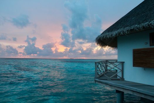 A beautiful overwater bungalow at sunset with vibrant colors in the sky and ocean.