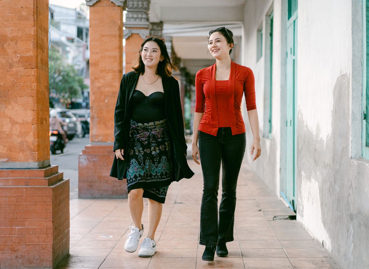 two smiling women walk down an urban sidewalk enjoying a sunny day in