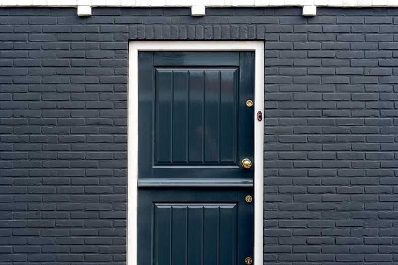 Close-up view of a stylish black exterior door with a brass handle, set within a brick wall facade.