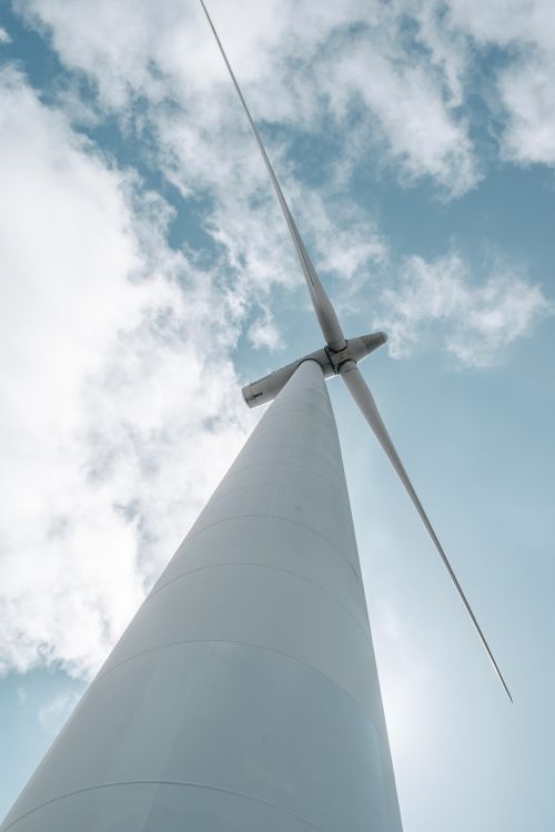 Free A towering wind turbine stands tall against a bright, partly cloudy sky. Renewable energy and sustainability concept. Stock Photo