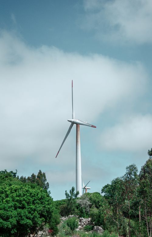 Free Scenic view of a wind turbine amidst a green landscape with blue sky. Stock Photo