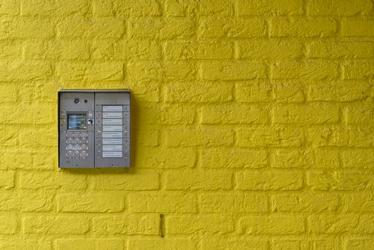A vibrant yellow brick wall featuring a modern intercom system, ideal for security or design concepts.