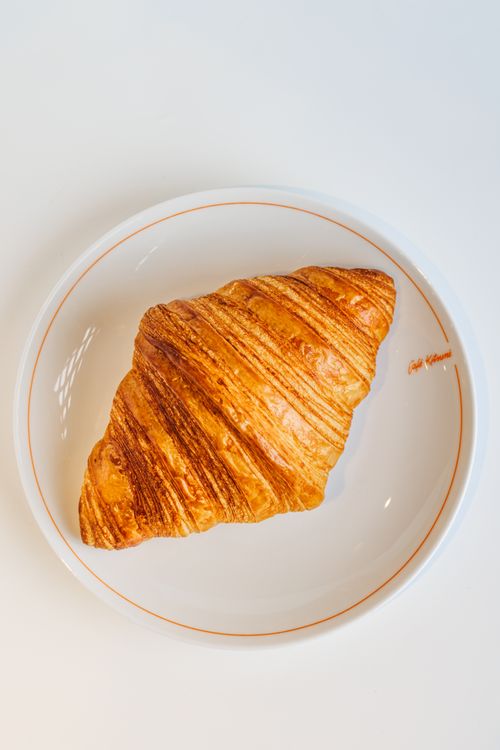 Free A golden, flaky croissant beautifully displayed on a white plate, perfect for breakfast or brunch. Stock Photo