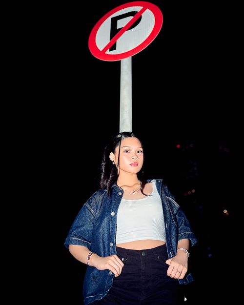 Free Stylish young woman posing confidently under a 'No Parking' sign against a night backdrop. Stock Photo