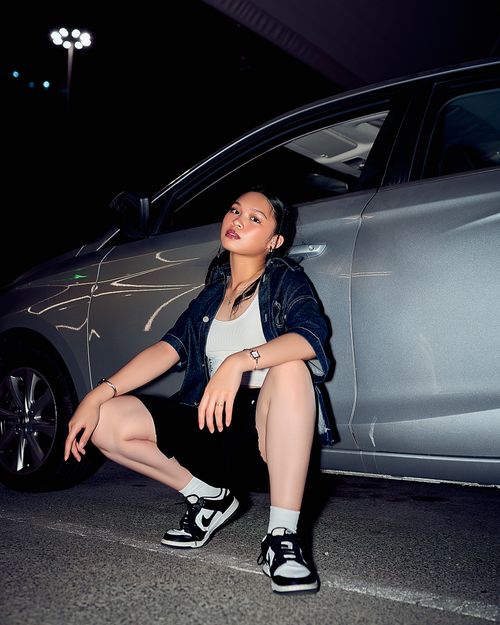 Free Confident woman in streetwear posing beside a car under night lights. Stock Photo