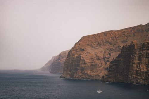 Free Dramatic coastal cliffs tower over the serene ocean under a hazy sky, capturing nature's grandeur. Stock Photo
