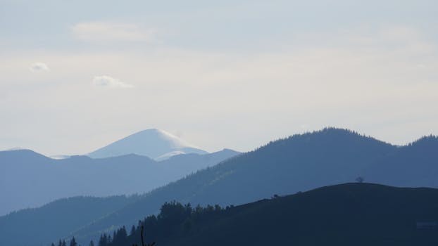 A tranquil view of mountains under a clear, soft blue sky with gentle lighting.