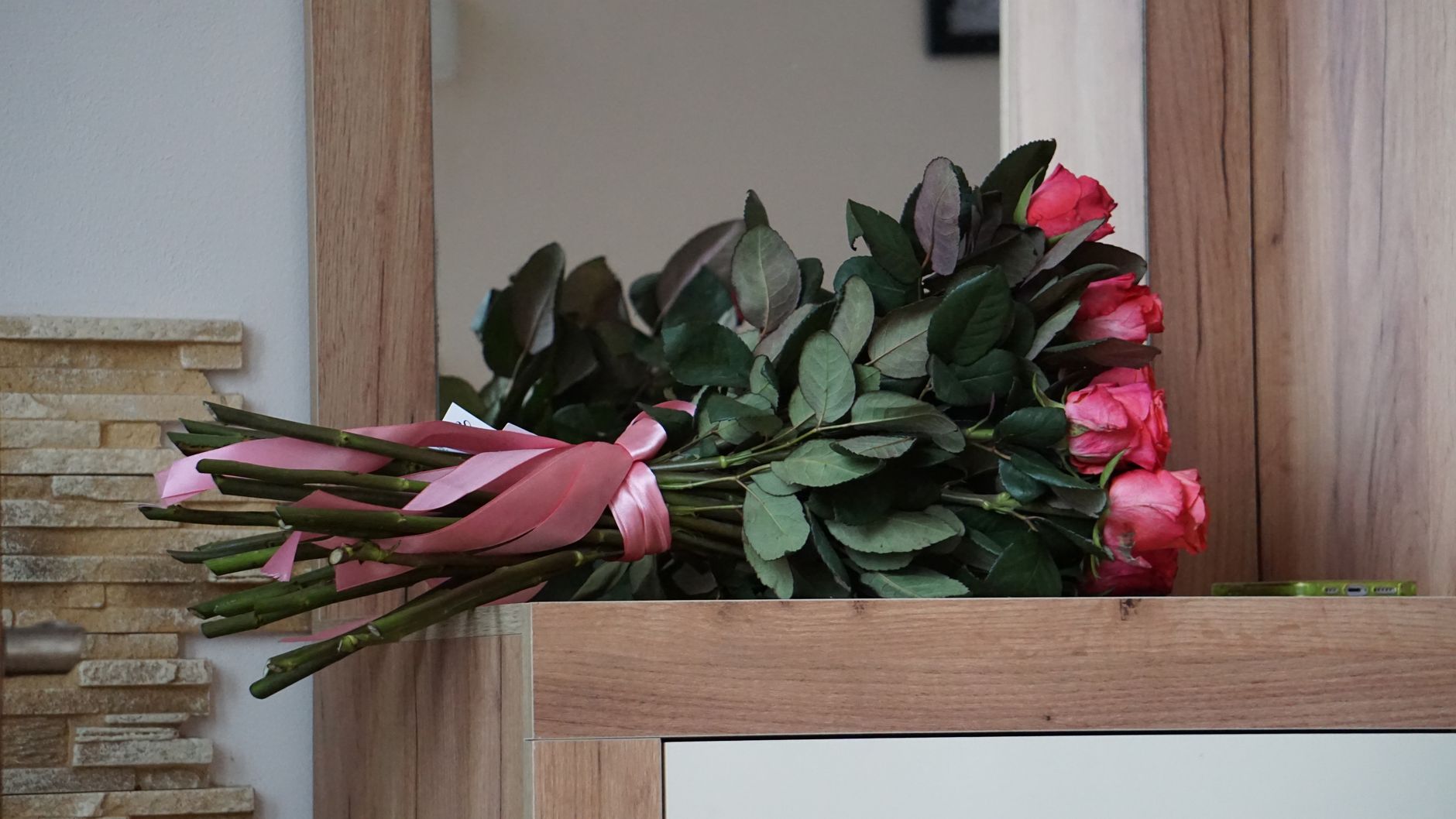 A charming bouquet of pink roses wrapped in a pink ribbon rests elegantly on a wooden surface indoors.