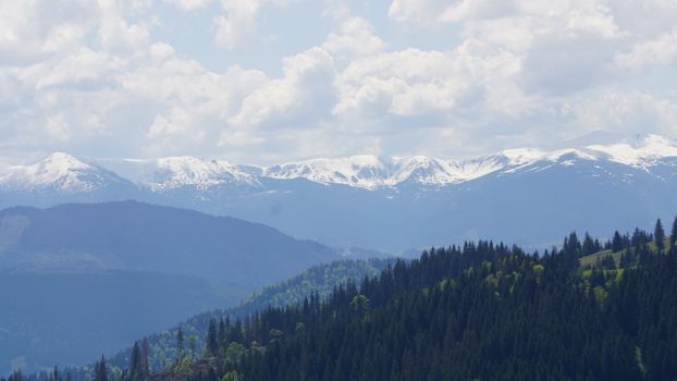 Breathtaking view of snow-capped mountains under a cloudy sky, surrounded by lush forests.