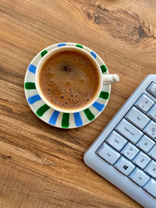 Free Cup of coffee beside a keyboard on a rustic wooden desk. Cozy office vibe. Stock Photo