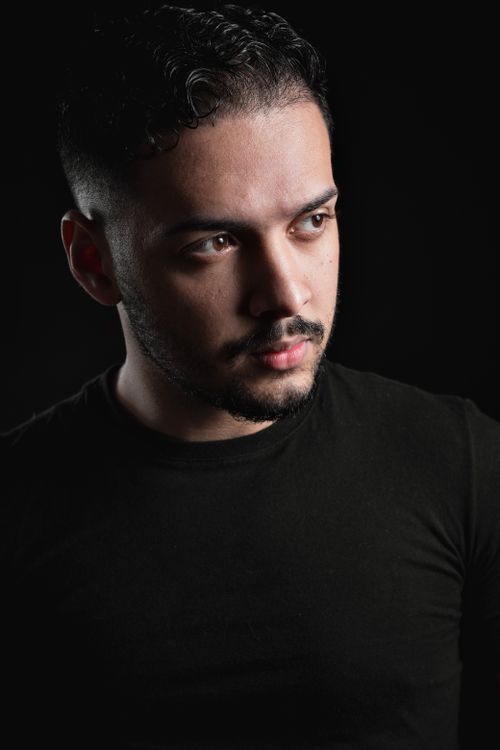 Free Side profile of a young man in a black shirt with a thoughtful expression against a dark background. Stock Photo