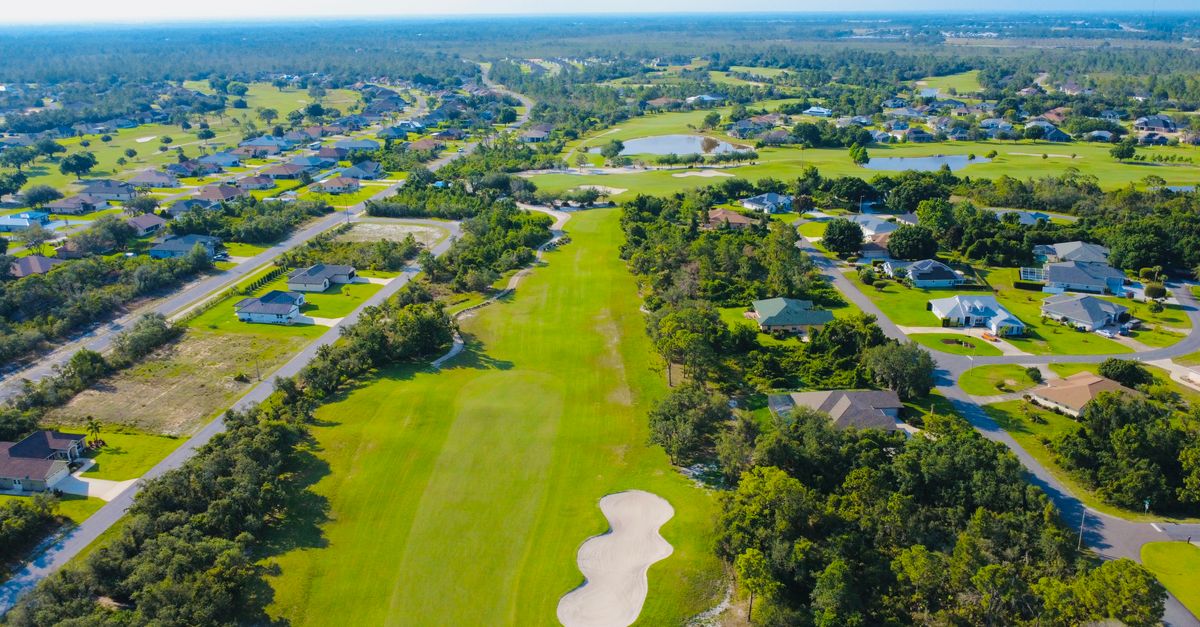 Beautiful aerial view of a suburban golf course with lush greenery and homes in the distance.