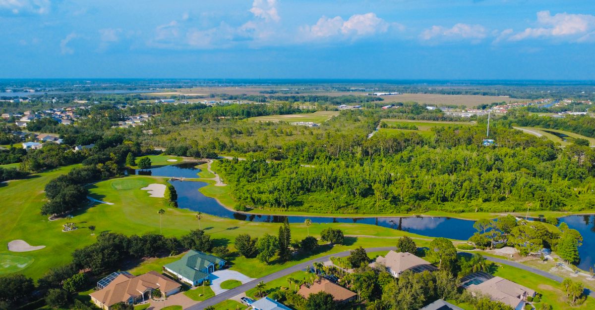 Aerial view of a lush green golf course and suburban homes in Florida under a clear blue sky.