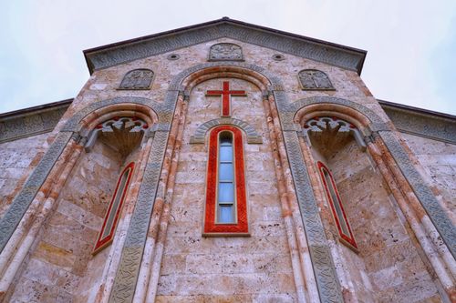 Free Close-up of an ornate church facade featuring a red cross and arched windows. Stock Photo
