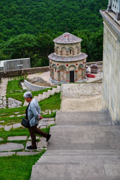 Free A person descends steps with a historic church set against lush greenery. Stock Photo