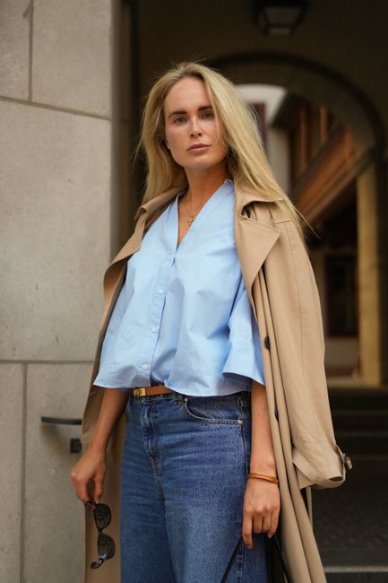 Fashionable woman wearing trench coat and denim stands in a city street.