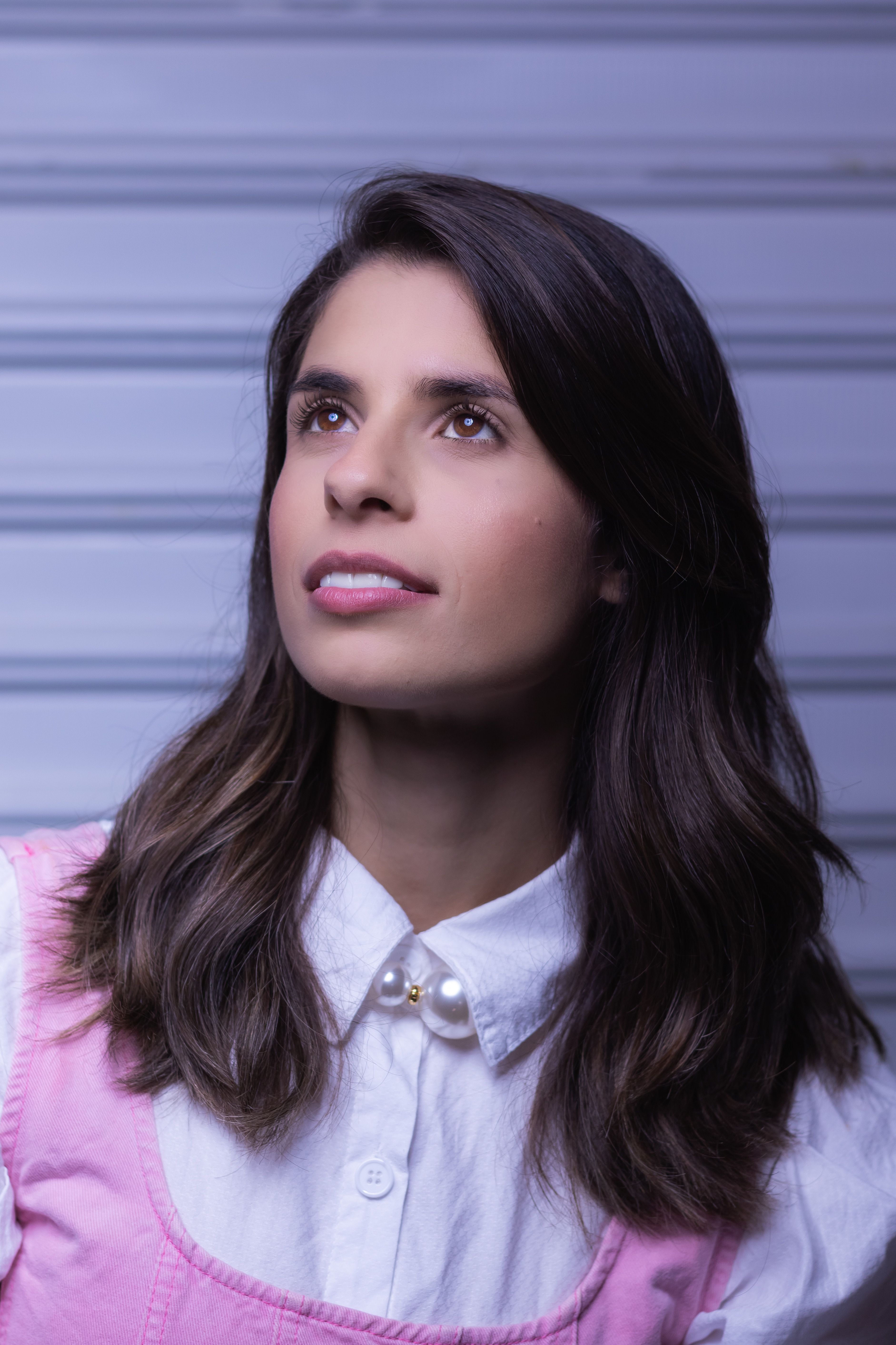 Young woman looking upward with a hopeful expression indoors against a striped background.