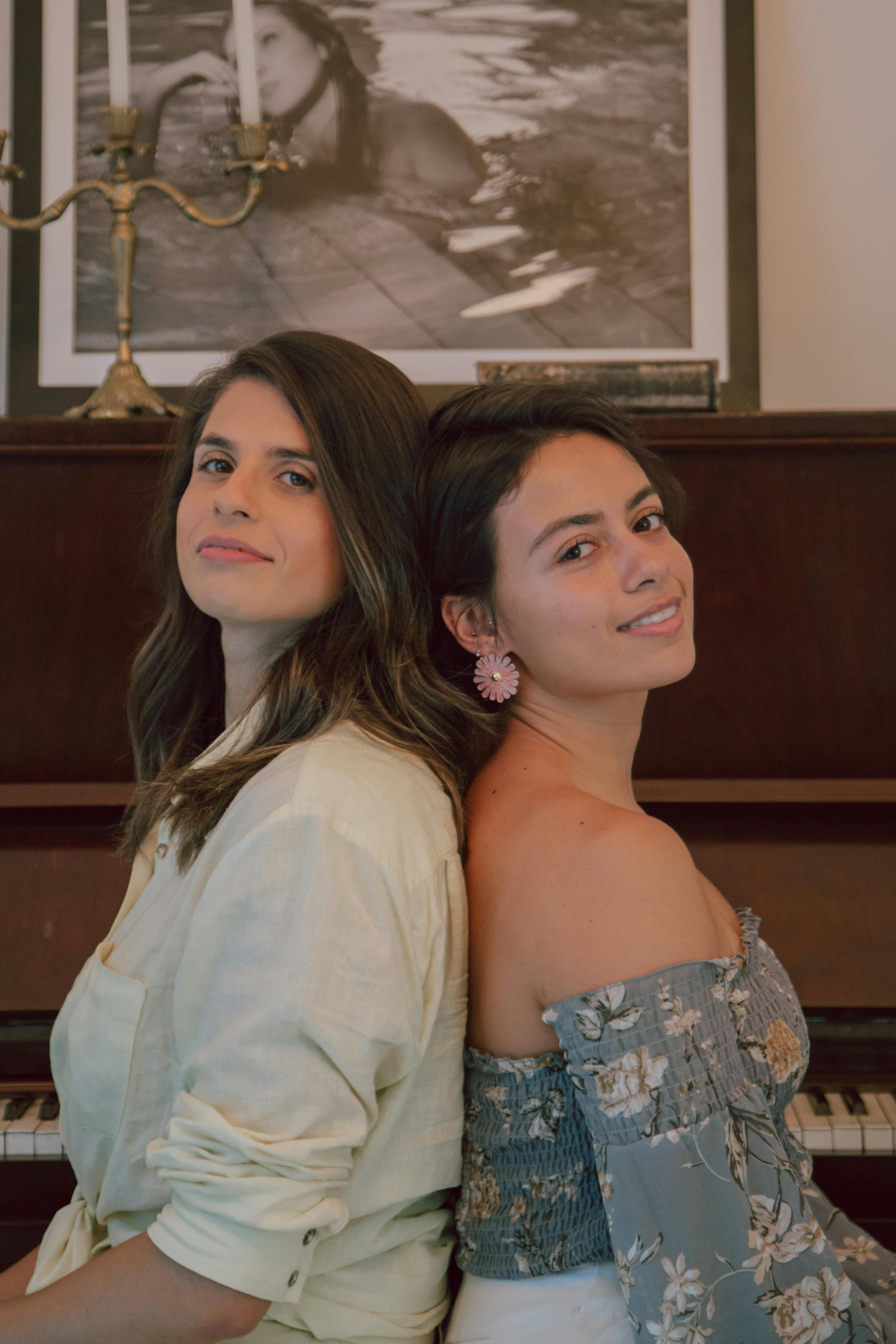 Free Two women sitting back-to-back in a stylish indoor setting with decor. Stock Photo