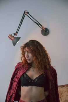 A fashionable young woman posing indoors with an artistic wall lamp behind her.
