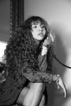 Black and white portrait of woman with curly hair using a vintage rotary phone.