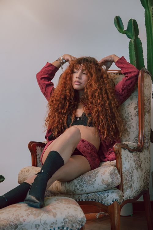 Free Relaxed woman with curly hair in a stylish indoor setting, exuding confidence and modernity. Stock Photo
