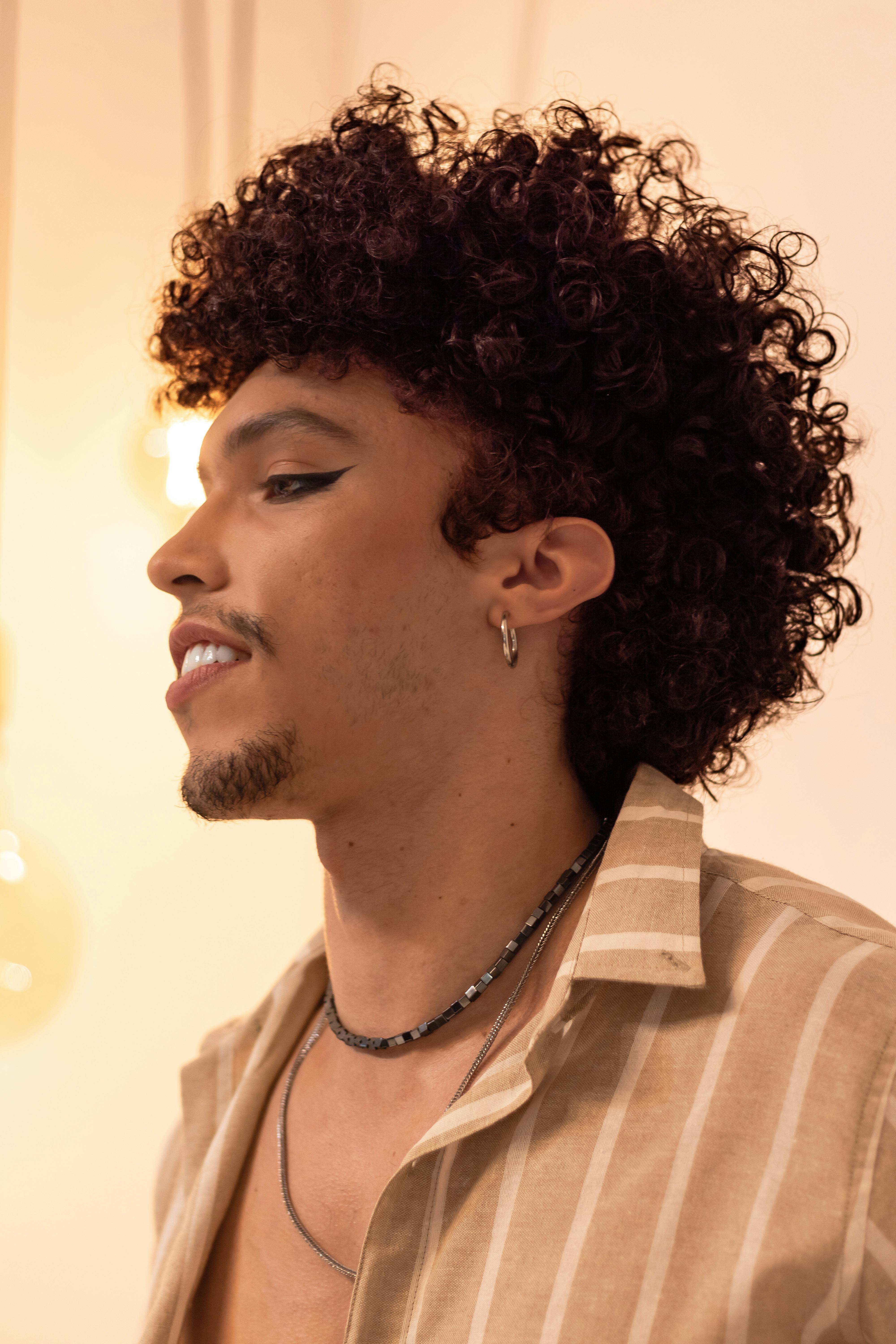 Side profile of a stylish man with curly hair and earrings indoors.
