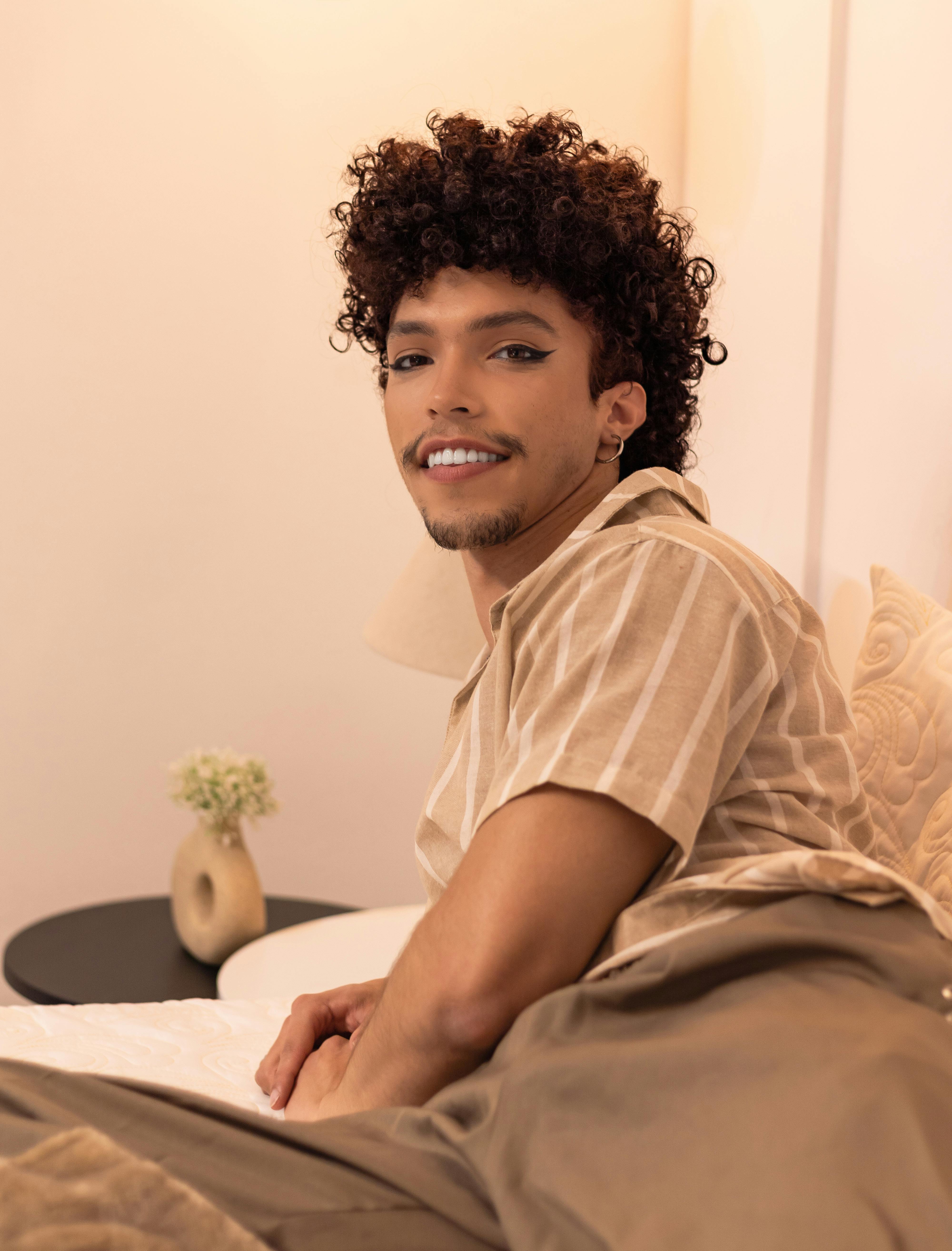 grátis Um jovem adulto sorrindo em um ambiente interno, deitado confortavelmente em uma cama, em um ambiente aconchegante e acolhedor. Foto profissional