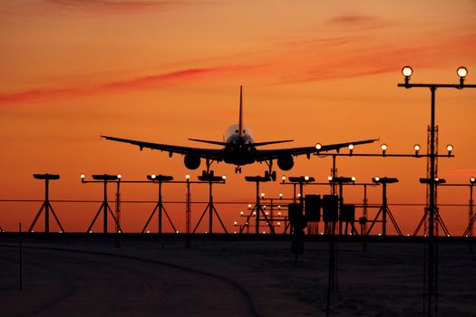 A silhouette of an airplane landing at sunset, capturing the vivid sky and runway lights.