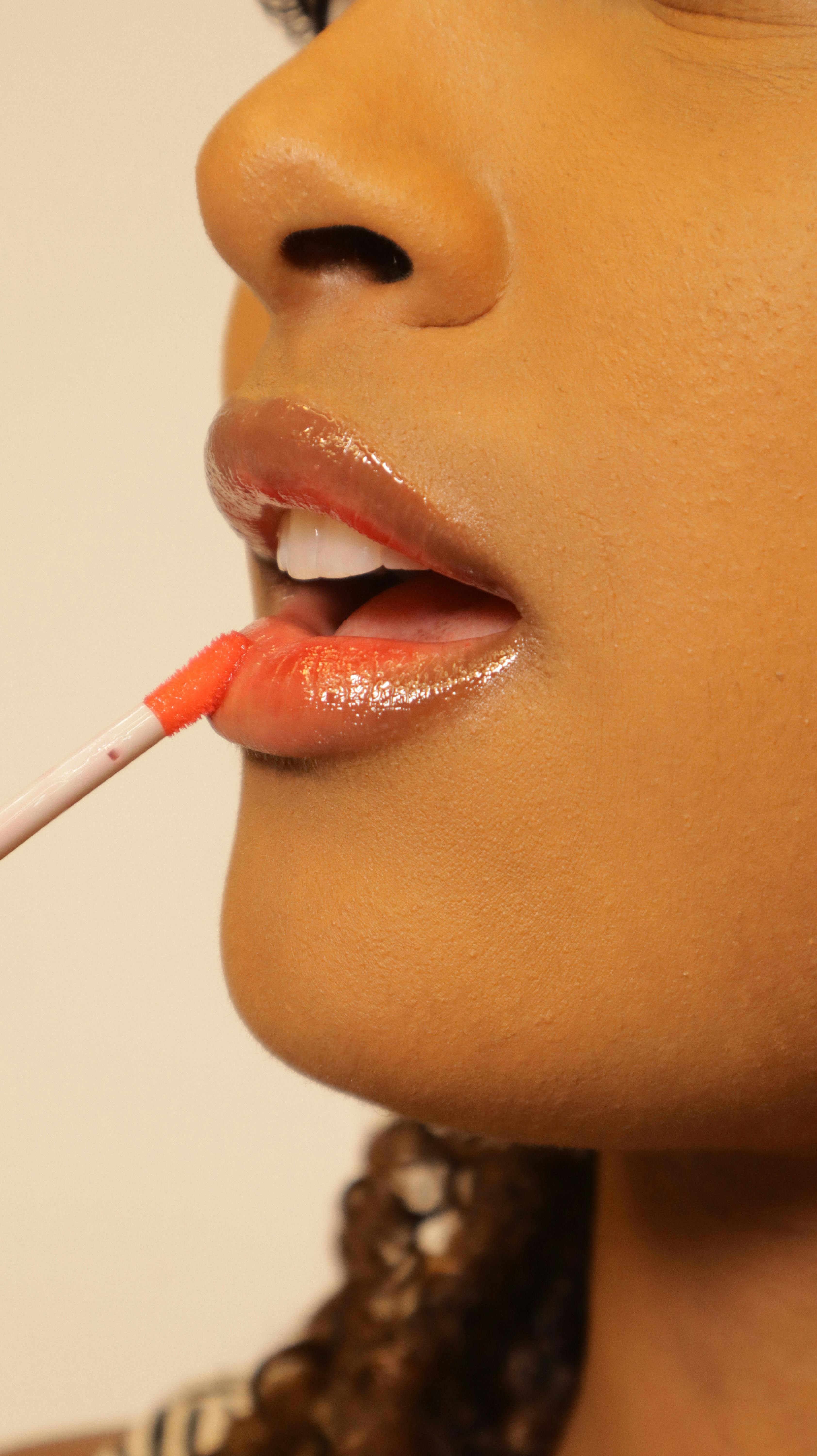 Side profile of a woman applying coral lip gloss enhances her lips, capturing a beauty routine.