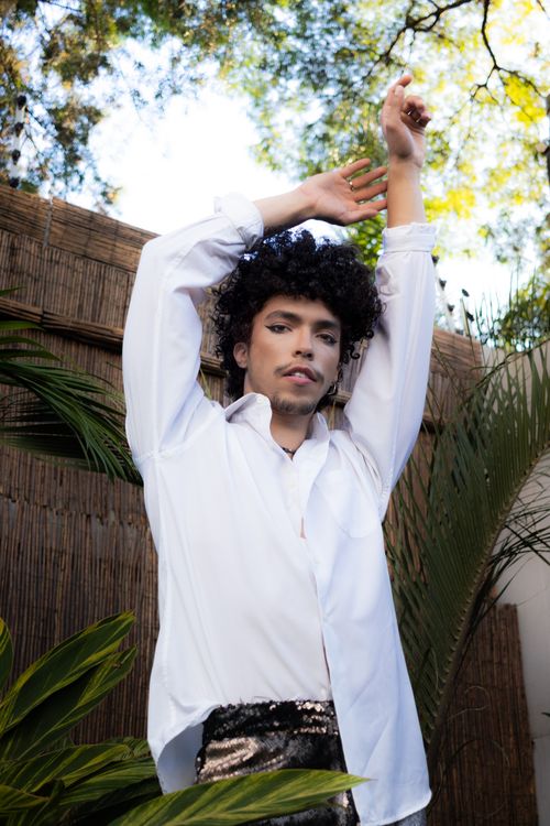 Free A young man in a white shirt poses fashionably outdoors with plants and natural light. Stock Photo