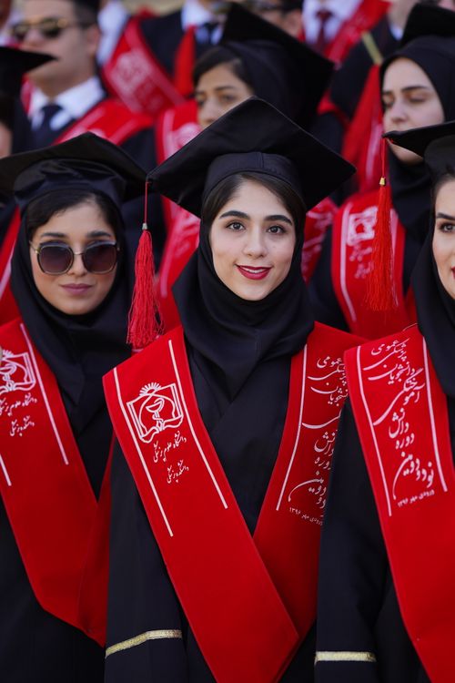 Free Women graduates celebrating at a ceremony in Iran, wearing red sashes and hijabs. Stock Photo