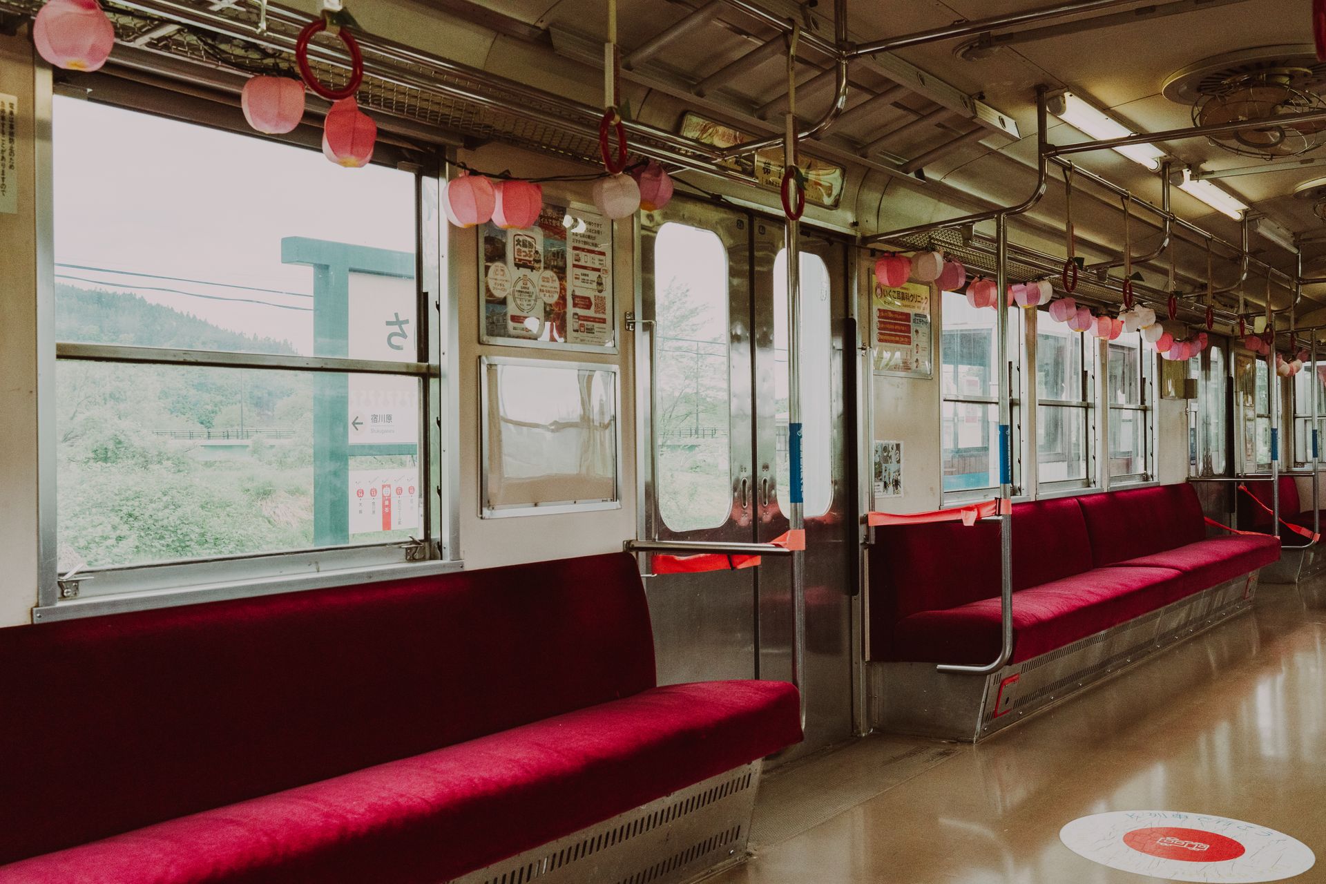 Interior view of an empty train carriage featuring red seats and decorative lanterns.