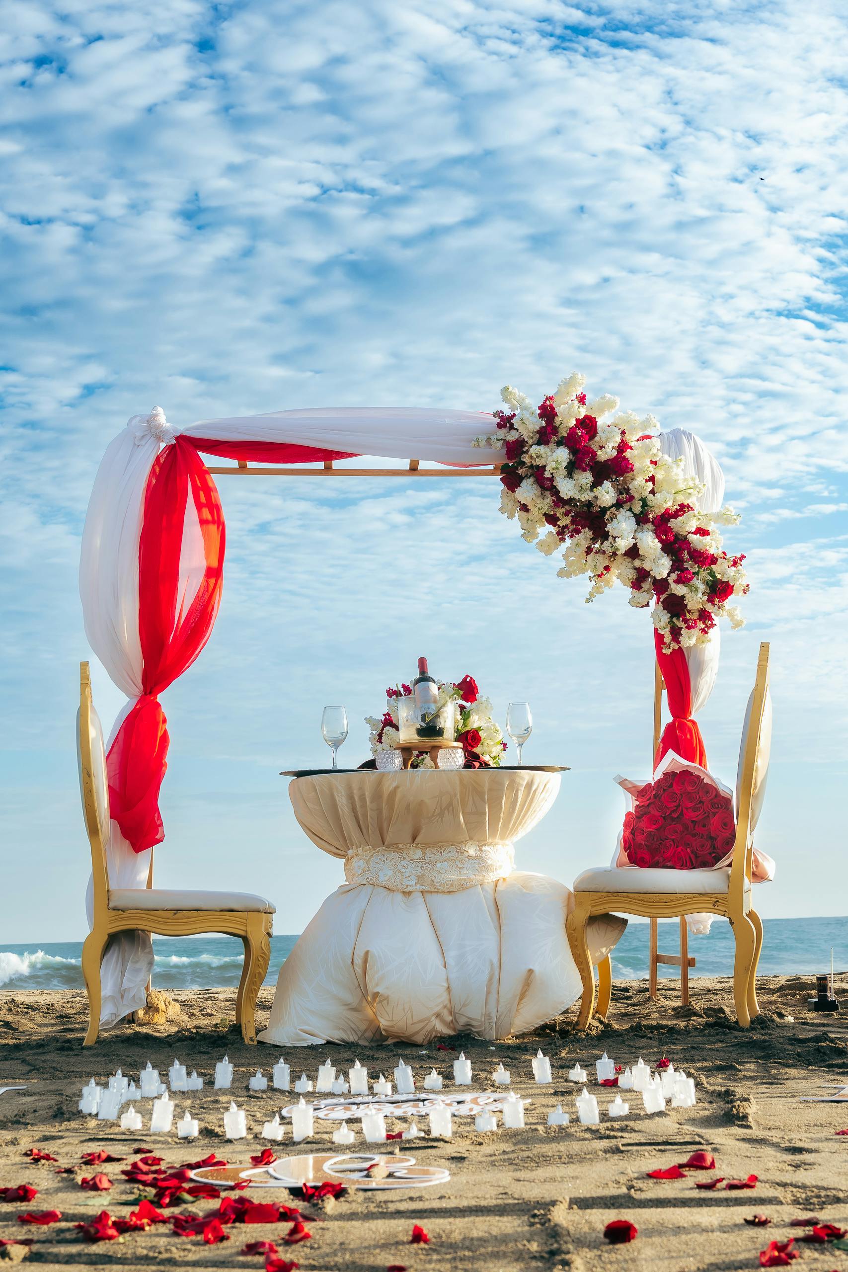 Beautiful romantic beachfront wedding setup with floral arch and elegant decorations in daylight.