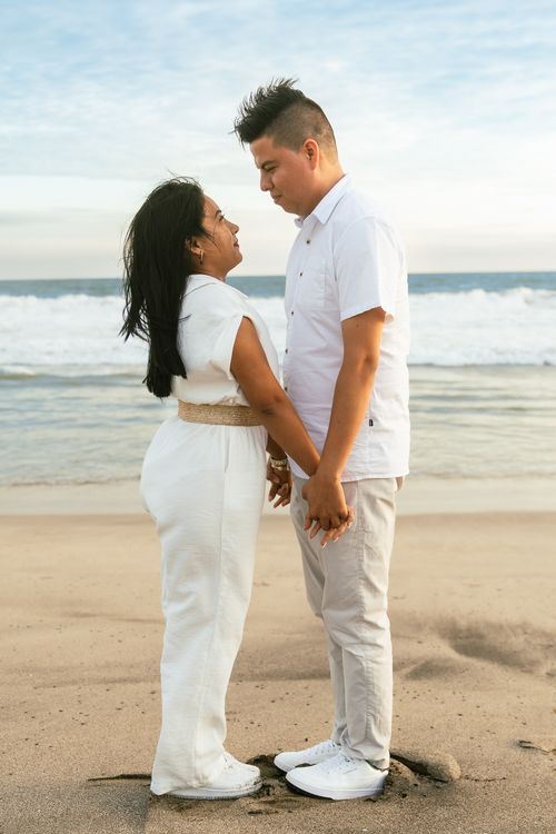 Free A romantic couple holding hands on a sunny beach, facing each other with love. Stock Photo