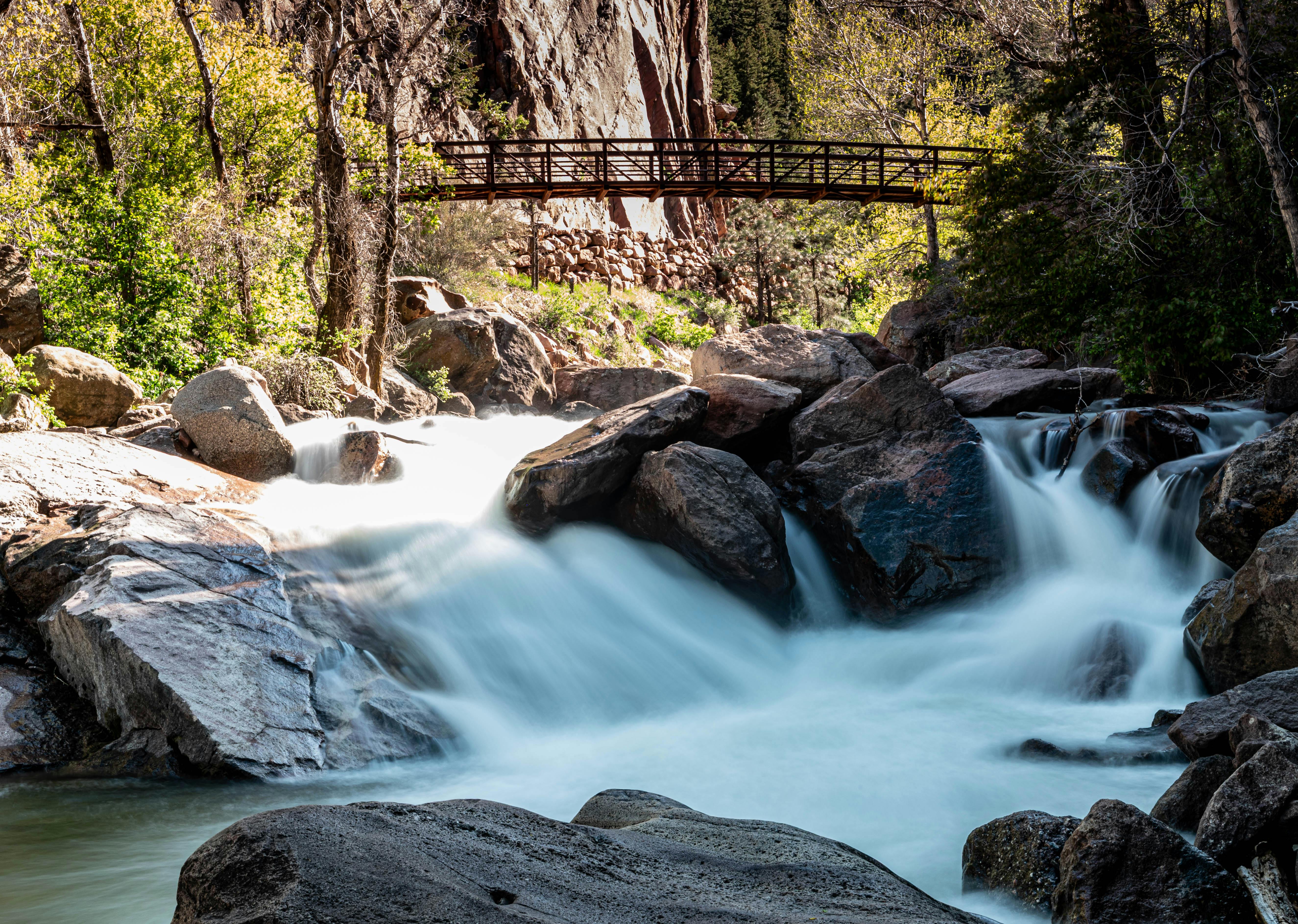 A serene waterfall flowing under a wooden bridge in a lush forest landscape.