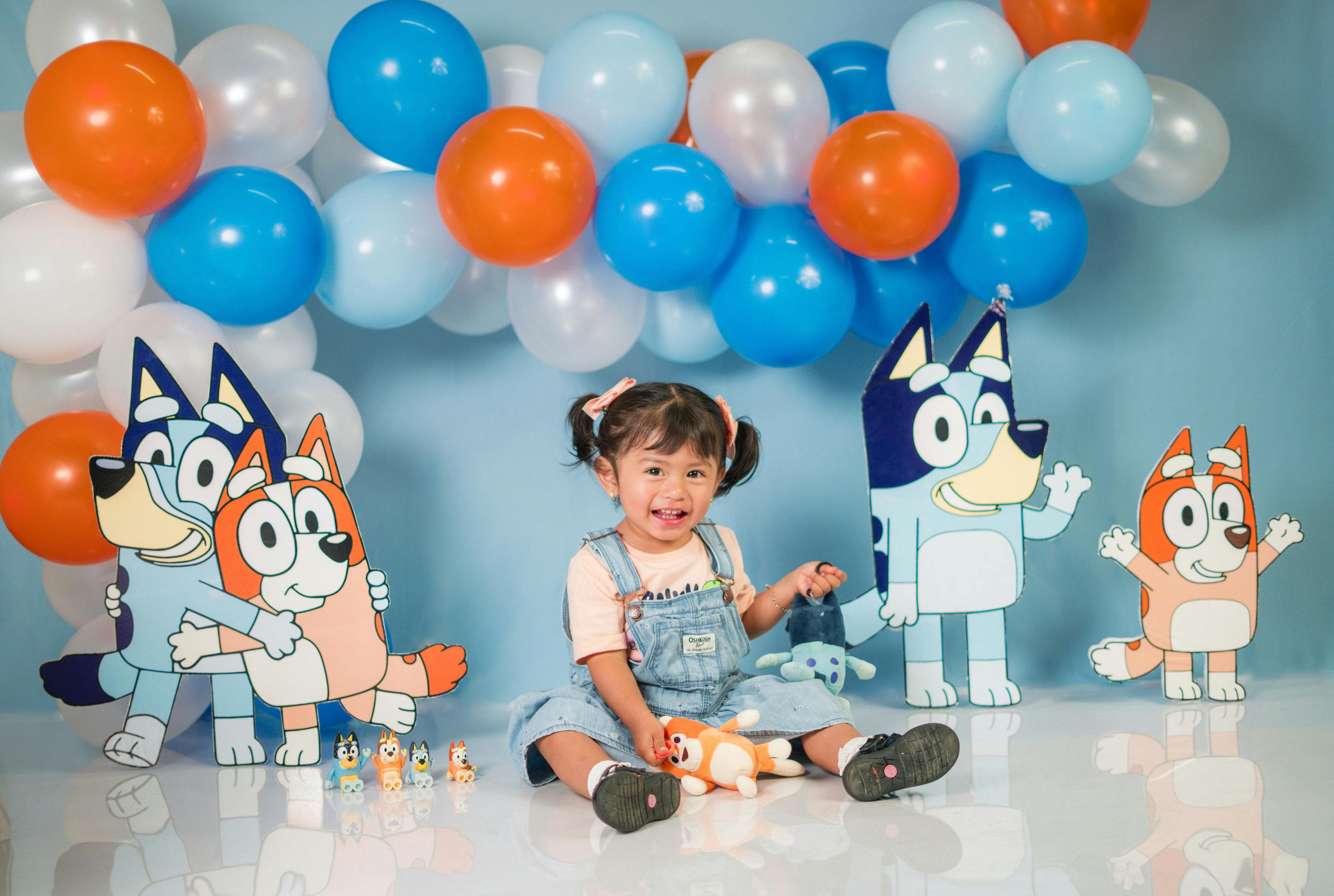 Cheerful child sitting among cartoon characters and balloons at birthday party.