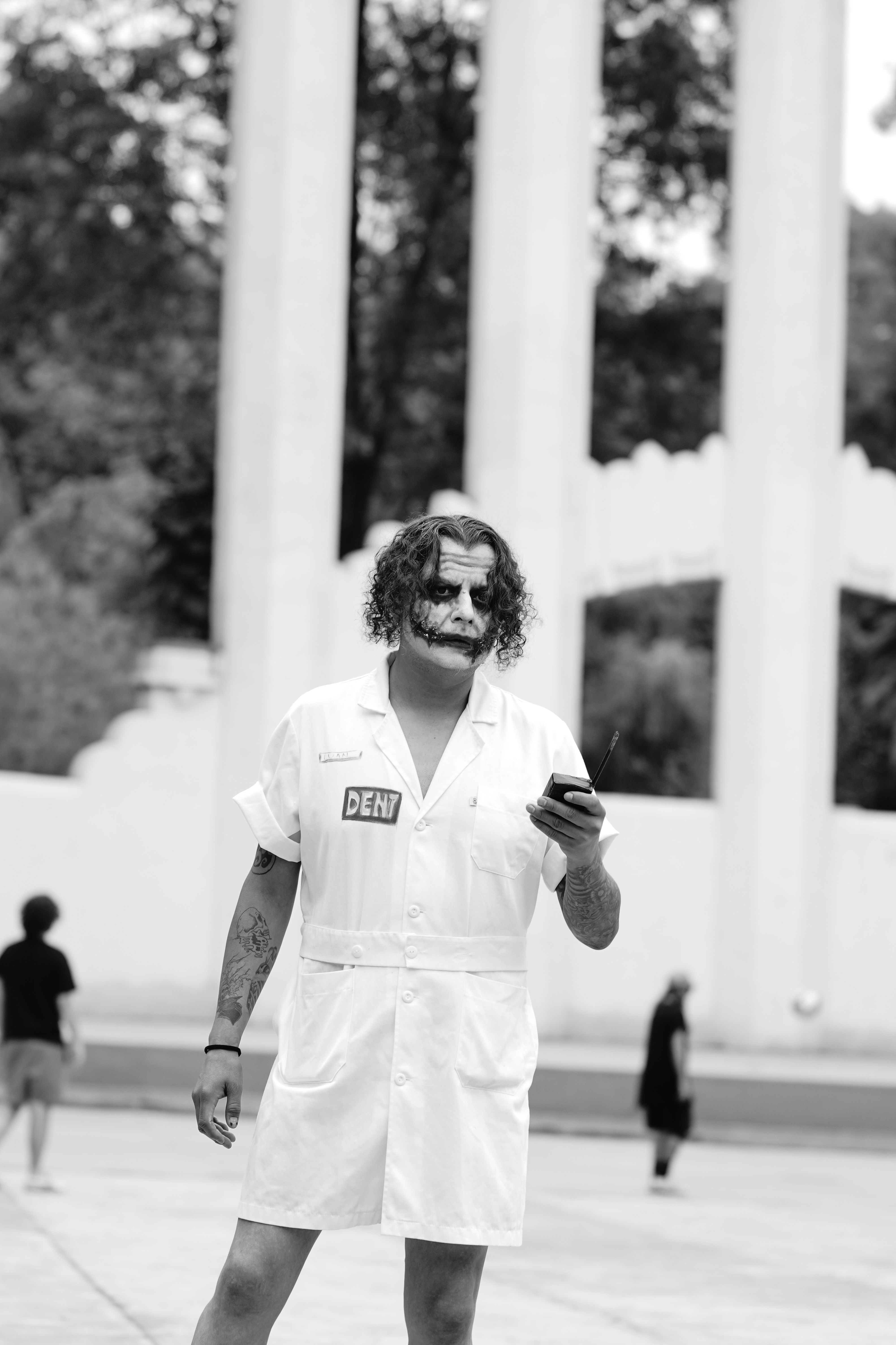 A person dressed in Joker makeup checks their phone in an outdoor urban setting.