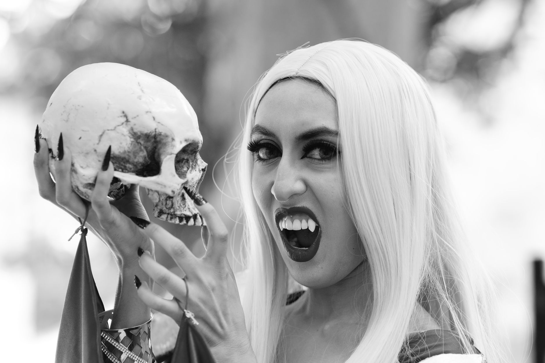 Black and white portrait of a vampire woman holding a skull, showcasing gothic Halloween style.