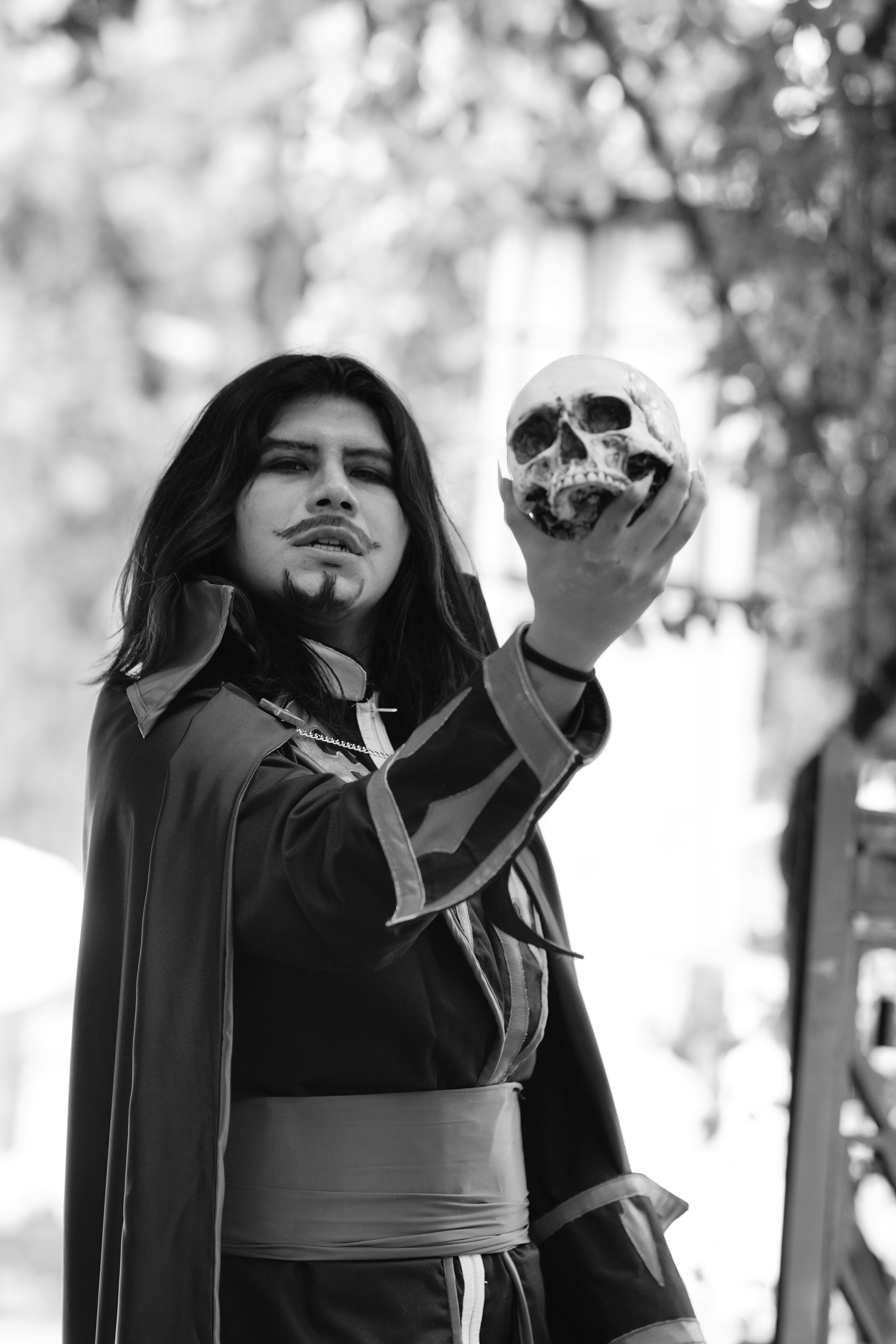 Free Black and white image of a costumed actor holding a skull, creating a dramatic and theatrical scene outdoors. Stock Photo