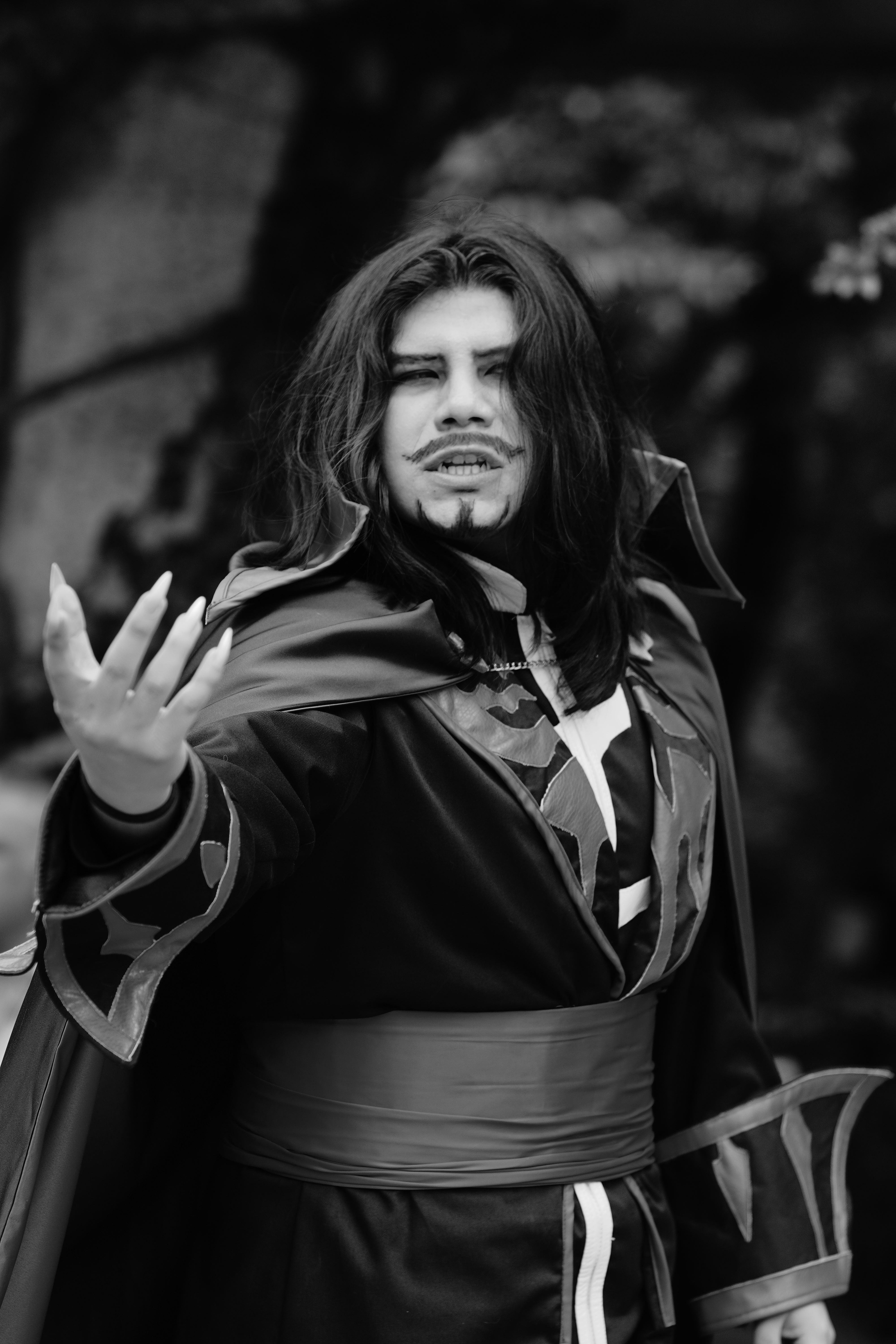 A dramatic black and white portrait of a fantasy character in a costume with long hair and a cape.