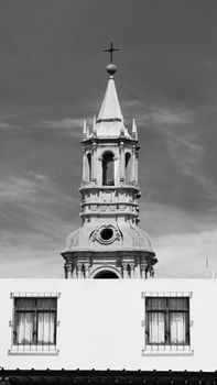 Black and white photo of a gothic church tower with a cross, capturing architectural beauty.