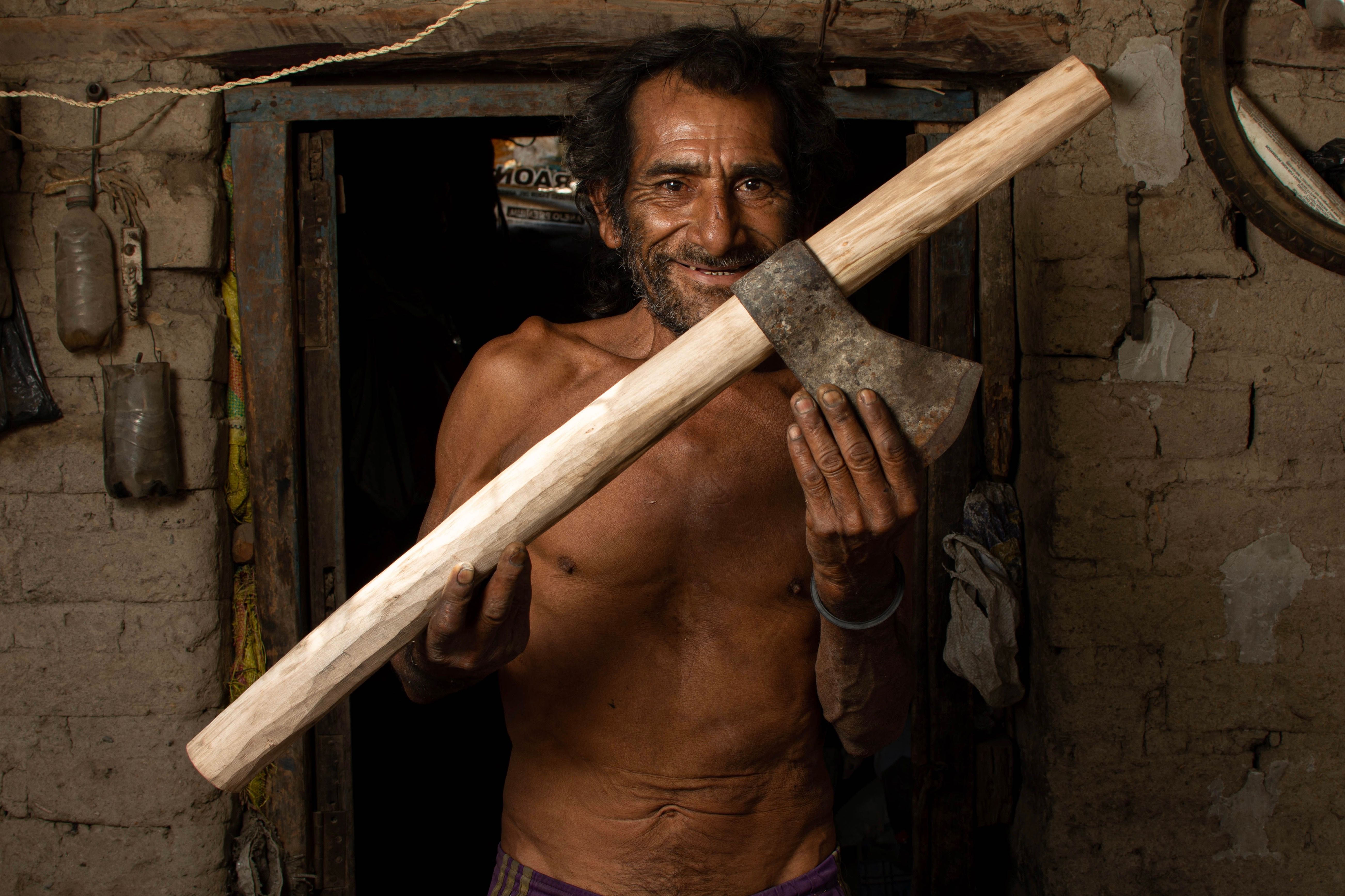 Senior artisan in Piura, Perú, proudly holds his handcrafted axe, showcasing rural craftsmanship.