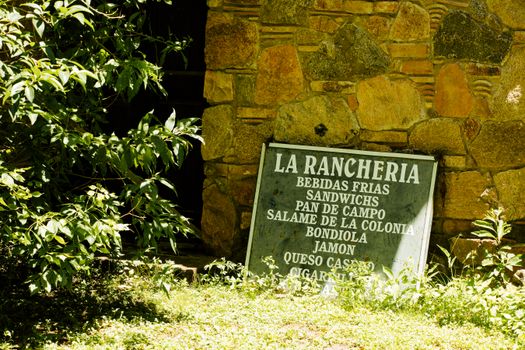 Rustic stone wall with a weathered sign at La Rancheria, a quaint spot in Córdoba, Argentina.