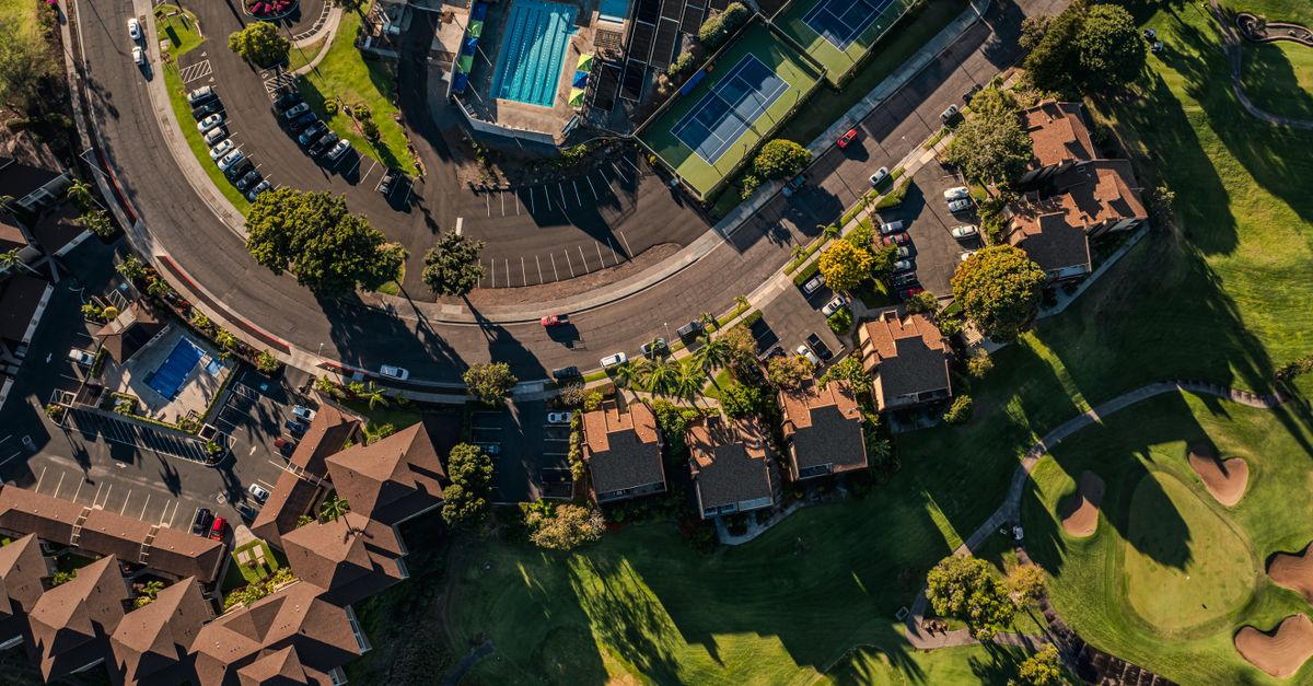 Stunning aerial shot of a Hawaiian residential area featuring tennis courts and a swimming pool surrounded by lush greenery.