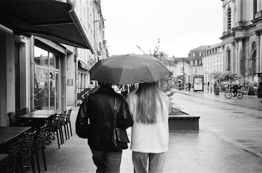 Black and white photo of a couple sharing an umbrella on a rainy day in France.