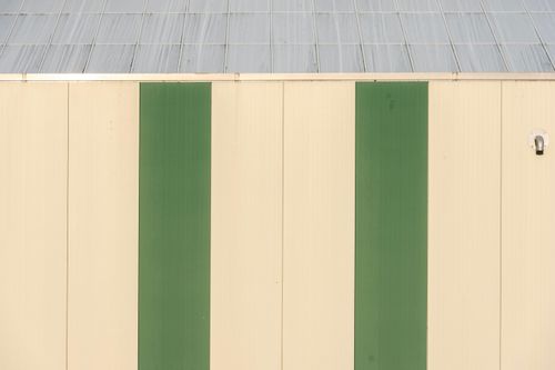 Free A minimalist industrial building facade featuring vertical green stripes and metal roof. Stock Photo