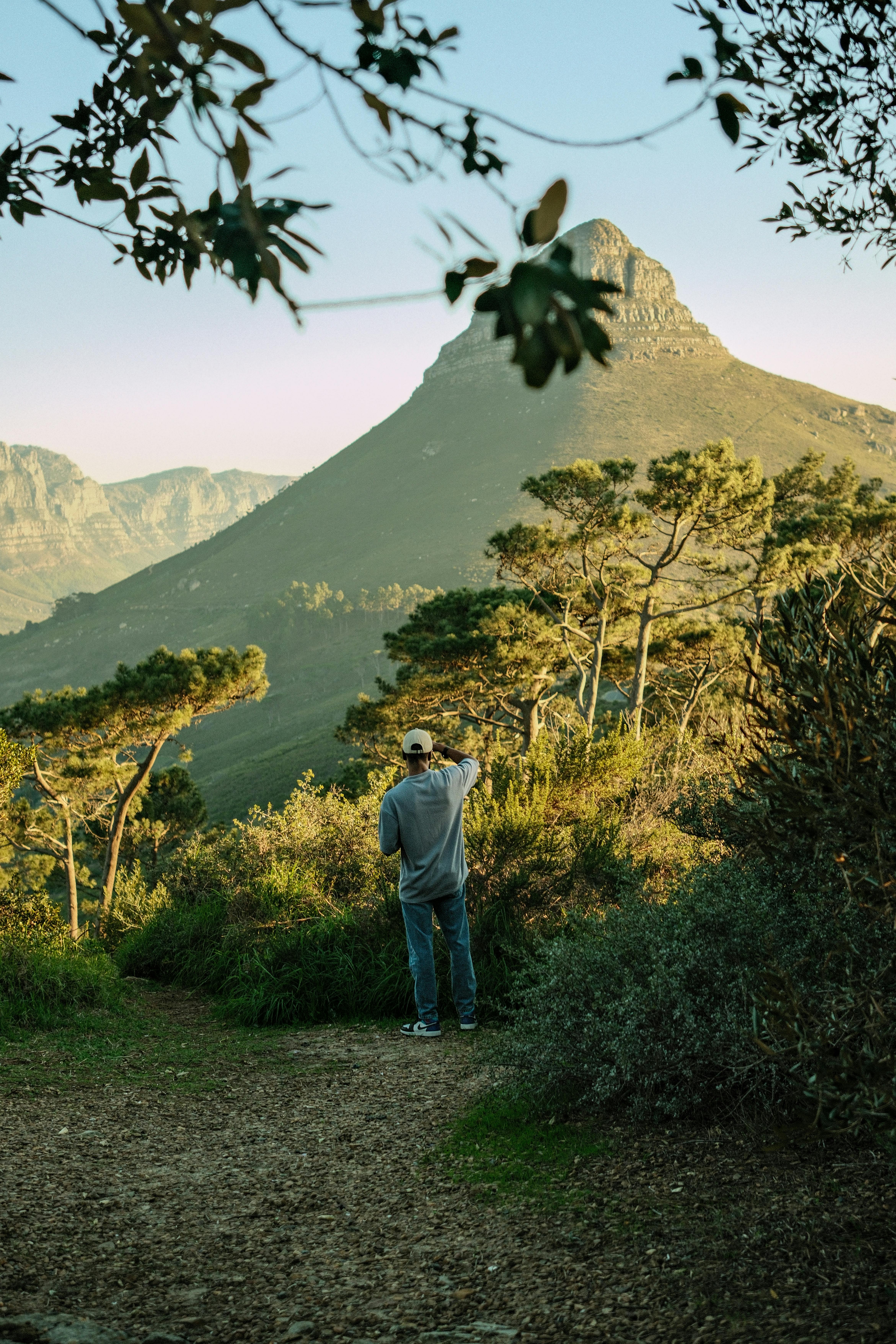 A person stands on a trail admiring the mountain view under a clear sky.