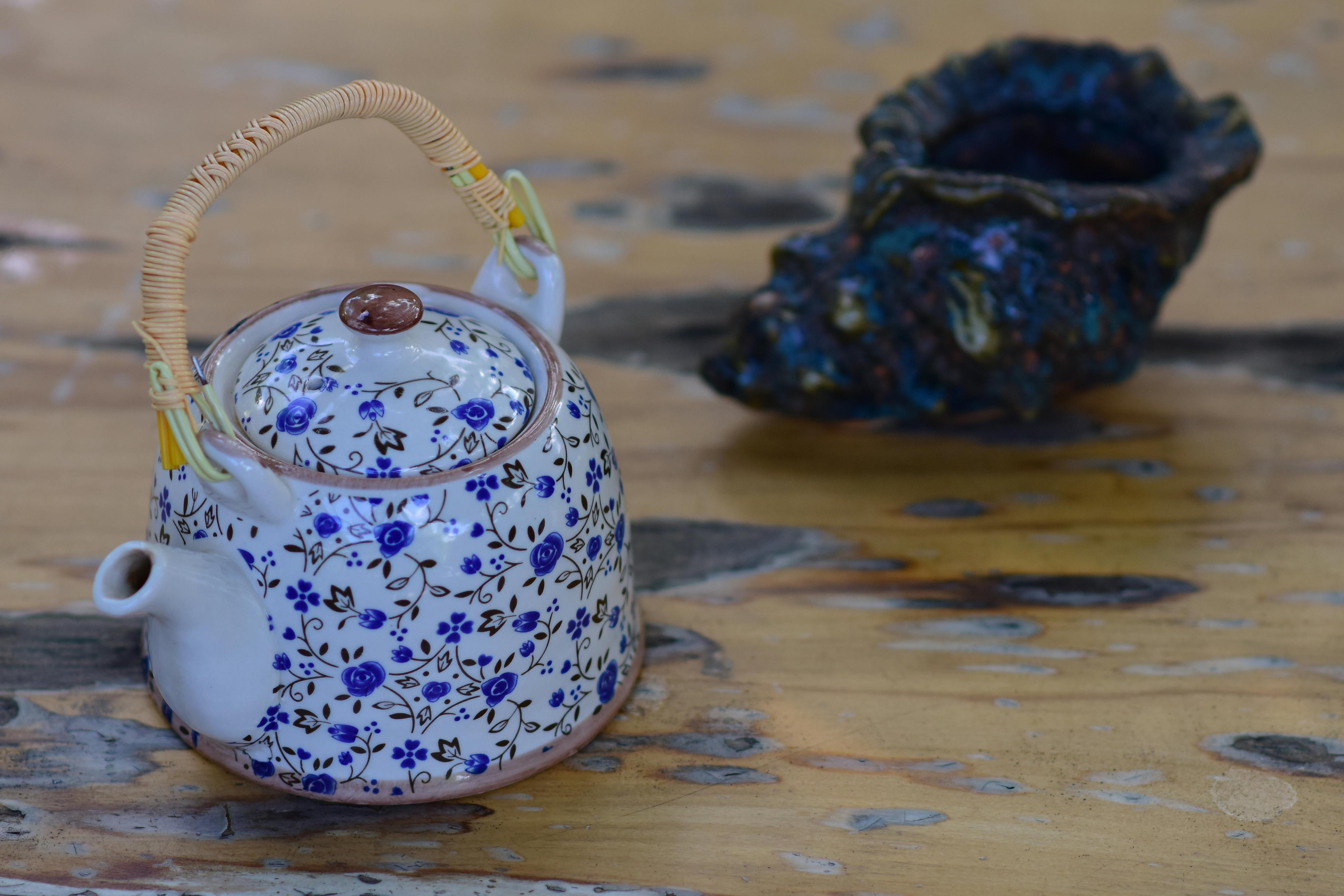 Artistic floral ceramic teapot and textured vase on a wooden table, featuring intricate patterns.